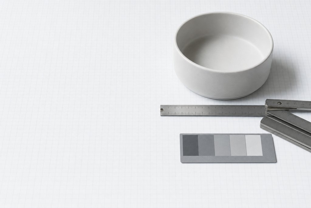 A plain ceramic bowl on graph paper beside a folding steel rule and a grey reference card