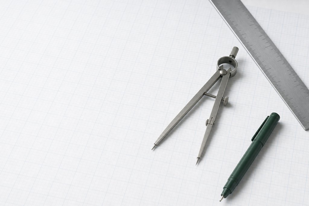 Draughtsman's dividers, a steel rule and a green fineliner resting on graph paper